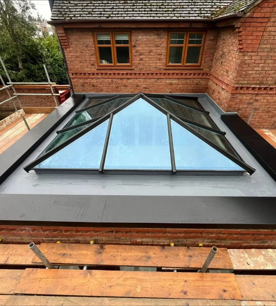 Anthracite aluminium roof lantern finished on a grey fibreglass flat roof beside the house
